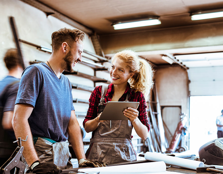 A man and woman holding a notepad, smiling and engaged in a discussion in a garage